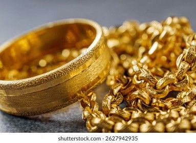 Närbild på en bred guldring och en grov guldkedja på en mörk yta.